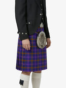Person wearing a purple plaid kilt with a black jacket and white knee-high socks on a white background