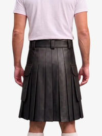 A person shown from the back wearing a black pleated leather kilt with side cargo pockets, paired with a light pink t-shirt and white socks, against a plain light gray background.