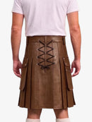 A brown faux-leather pleated kilt with a lace-up back closure, shown on a model from the back wearing a white t-shirt and white socks against a light gray background.