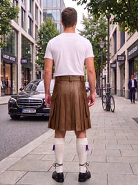 A man viewed from behind wearing a brown pleated leather kilt, white t-shirt, white knee-high socks with purple tassels, and black shoes, standing on a city street.