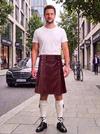 A man stands on a city sidewalk wearing a black leather kilt, white t-shirt, white knee-high socks, and black leather shoes. A black Mercedes-Benz car is parked on the street behind him, with buildings, trees, and a bicycle in the background.