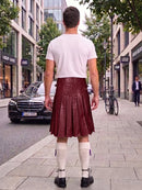 A man standing on a city sidewalk, viewed from behind, wearing a white t-shirt and a dark red leather kilt with white knee-high socks and black shoes.