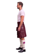 A man shown in profile wearing a dark burgundy leather kilt with multiple utility pockets, a white t-shirt, white socks, and black leather shoes, set against a plain white background.