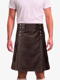 A man wearing a dark brown faux-leather kilt with silver-tone metal hardware and side pockets, paired with a light pink t-shirt and white socks, shown from the chest down against a white background.