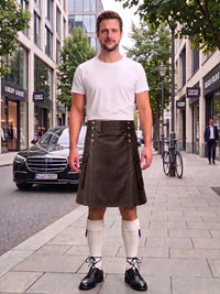A man stands on a city sidewalk wearing a black leather kilt, white t-shirt, white knee-high socks, and black leather shoes. A black Mercedes-Benz car is parked on the street behind him, with buildings, trees, and a bicycle in the background.