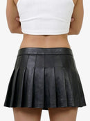 Person wearing a black pleated skirt and white top on a plain background
