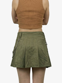 Person wearing a green skirt with zippers and a brown top on a white background