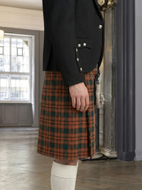 Person wearing a black jacket and orange plaid kilt indoors.
