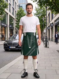 A man stands on a city sidewalk wearing a dark green kilt with white geometric stripe details, a white t-shirt, white knee-high socks, and black leather shoes. The background shows a blurred urban street scene with buildings, a parked black car, and a bicycle.