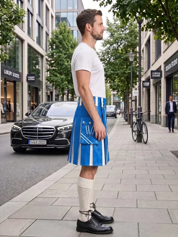 A man standing on a city sidewalk wearing a white short-sleeve T-shirt, a bright blue and white vertically striped kilt with front pockets, cream knee-high socks, and black leather shoes. A black Mercedes-Benz car and urban buildings are visible in the background.