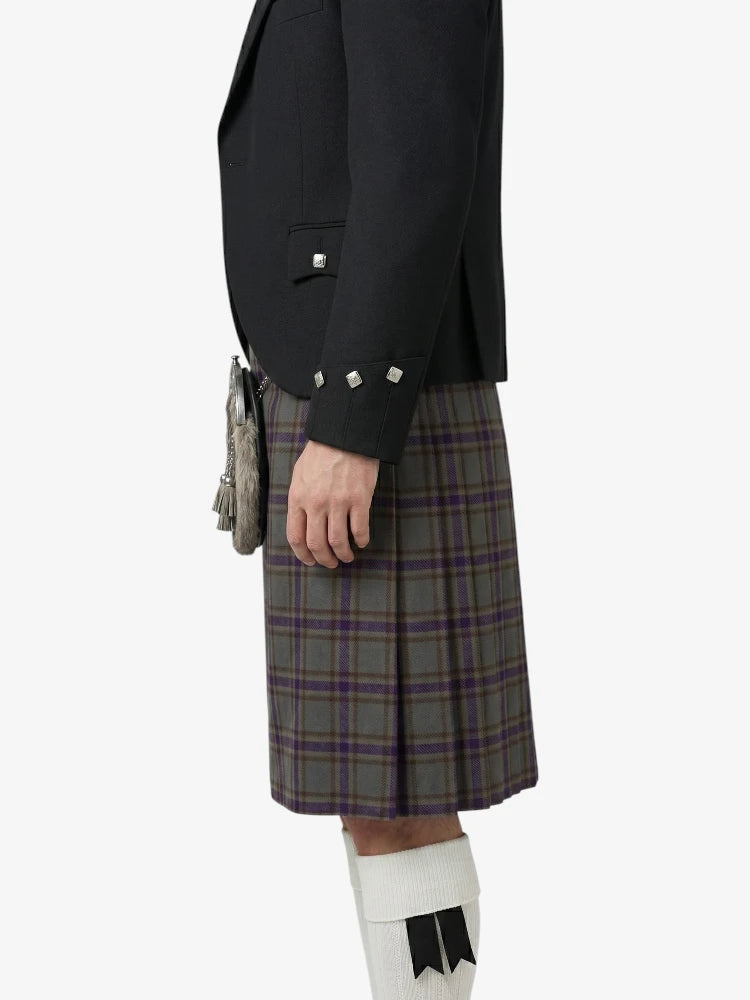Person wearing a black blazer and plaid kilt on a white background
