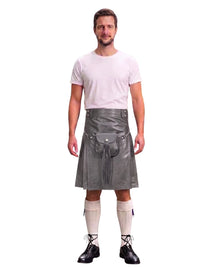 A man modeling a gray faux-leather kilt with a matching belt and pouch, paired with a white t-shirt, cream knee-high socks, and black lace-up shoes, against a plain white background.