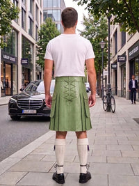 A man viewed from behind wearing a light green leather kilt with lace-up back detailing, a white t-shirt, white knee-high socks, and black shoes, standing on a city sidewalk.