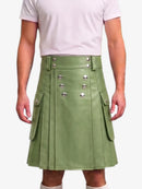 A person wearing a sage green faux-leather kilt with silver-tone decorative buttons and side flap pockets, paired with a light pink t-shirt against a plain white background.
