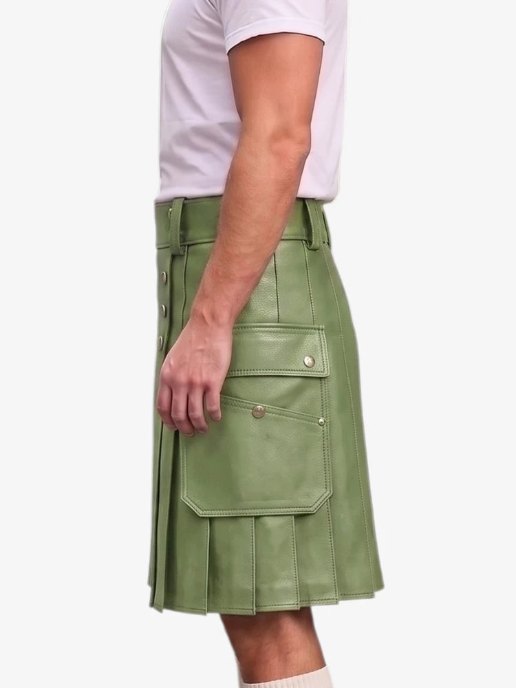 A side view of a person wearing a sage green faux-leather kilt with flap pockets and gold-tone hardware, paired with a white t-shirt against a light gray background.