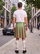 A man viewed from behind wearing a light green pleated kilt with red vertical stripes, a white t-shirt, white knee-high socks, and black shoes, standing on a city sidewalk.