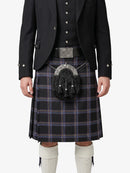 Person wearing a black jacket, plaid kilt, and white knee-high socks on a white background