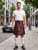 A man stands on a city sidewalk wearing a white crew-neck t-shirt and a dark brown leather kilt with white geometric line details. He is also wearing white knee-high socks and black leather shoes.