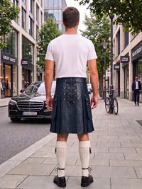 A man standing on a city sidewalk, viewed from behind, wearing a dark navy blue leather kilt with lace-up back detailing, a white t-shirt, cream knee-high socks, and black shoes.