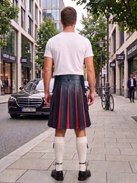 A man viewed from behind wearing a white t-shirt and a black leather pleated kilt with red center panels, standing on a city sidewalk.