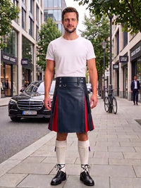 A man stands on a city sidewalk wearing a white crew-neck t-shirt and a black leather kilt with red side panels and silver metal hardware. He is also wearing white knee-high socks and black leather shoes.