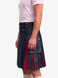 A man wearing a black faux-leather kilt with red pleated inserts and silver-tone hardware, paired with a light pink t-shirt and cream socks, against a plain white background.