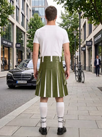 A man stands on a city sidewalk facing away from the camera, wearing an olive green pleated kilt with white vertical stripe panels, a white t-shirt, white knee-high socks, and black shoes. Storefronts, trees, and parked cars are visible in the background.