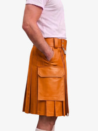 A person wearing a tan leather kilt with pleated detailing, a front flap pocket, and a matching belt, paired with a light pink t-shirt against a plain white background.