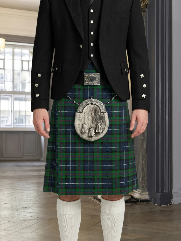 Person wearing a traditional Scottish kilt with a plaid pattern in a room with large windows.