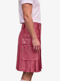 A person wearing a pink pleated leather kilt with silver snap buttons and a matching belt, paired with a white t-shirt, shown from the side against a light gray background.