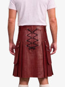 A person shown from the back wearing a dark red faux-leather pleated kilt with a black lace-up closure and side pockets, paired with a light pink t-shirt and white socks against a white background.