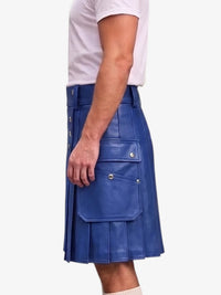 A man wearing a blue faux-leather kilt with pleated detailing and flap pockets, paired with a white t-shirt, shown from a side profile against a light gray background.