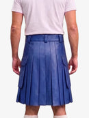 A person shown from the back wearing a blue pleated leather kilt with side flap pockets, paired with a light pink t-shirt and white socks, against a plain light gray background.