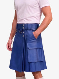 A man wearing a royal blue faux-leather kilt with a matching belt, silver metal grommets, and cargo pockets, paired with a light pink t-shirt against a white background.