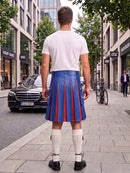 A man standing on a city sidewalk, viewed from behind, wearing a white t-shirt, a blue pleated leather kilt with red pleats, white knee-high socks, and black shoes. Buildings, trees, a black Mercedes, and a bicycle are visible in the background.