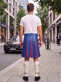 A man standing on a city sidewalk, viewed from behind, wearing a white t-shirt, a blue pleated leather kilt with red pleats, white knee-high socks, and black shoes. Buildings, trees, a black Mercedes, and a bicycle are visible in the background.