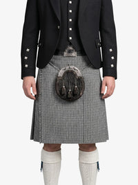 Person wearing a black jacket with white buttons, a kilt, and white knee-high socks on a white background