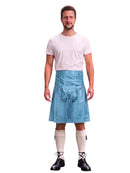 A man modeling a light blue denim kilt with a front flap pocket, paired with a white t-shirt, cream knee-high socks, and black lace-up boots, against a solid white background.