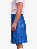 A man wearing a bright blue faux-leather kilt with silver snap buttons and flap pockets, paired with a white t-shirt, shown from a side profile against a light gray background.