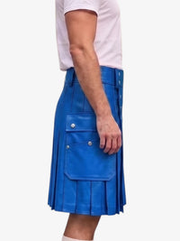 A person wearing a bright blue pleated leather kilt with flap pockets and silver-tone hardware, paired with a light pink t-shirt, shown from the side against a plain white background.