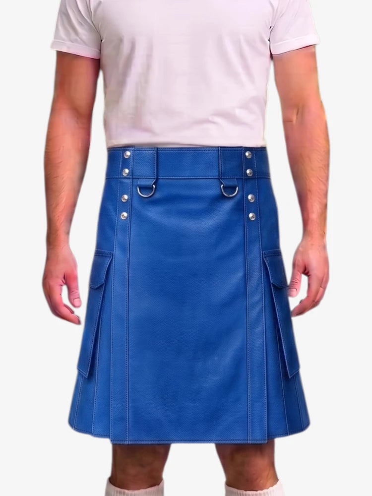 A man wearing a bright blue faux-leather kilt with silver-tone metal hardware, belt loops, and side pockets, paired with a light pink t-shirt and beige socks.