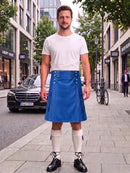 A man standing on a city sidewalk wearing a white crew-neck t-shirt and a bright blue leather kilt with silver metal grommets and a matching waist belt. He is also wearing white knee-high socks and black leather shoes.