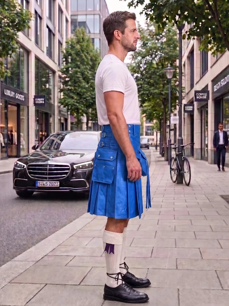 A man standing on a city sidewalk wearing a bright blue leather kilt, a white t-shirt, white socks, and black leather shoes. The background shows a street with a black Mercedes-Benz, trees, and storefronts.