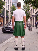 A man viewed from behind wearing a green leather kilt, white t-shirt, white knee-high socks, and black shoes, standing on a city sidewalk.