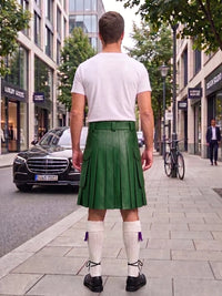 A man viewed from behind wearing a green leather kilt, white t-shirt, white knee-high socks, and black shoes, standing on a city sidewalk.