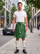 A man stands on a city sidewalk wearing a green kilt with white geometric stripe details, a white t-shirt, white knee-high socks, and black leather shoes. The background shows a blurred street scene with buildings, a black Mercedes-Benz car, and a bicycle.